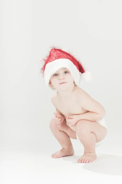 Adorable baby toddler girl squats wearing santa's hat and diapers — Stock Photo, Image