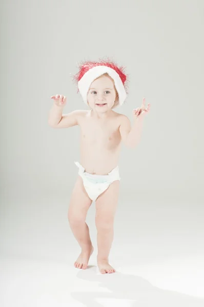 Glad söt baby barn flicka klädd i santa hatt och blöjor står — Stockfoto