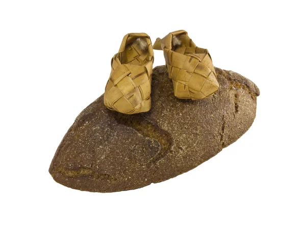 stock image Pair of wattled bast shoes on a piece of the rye bread, isolated