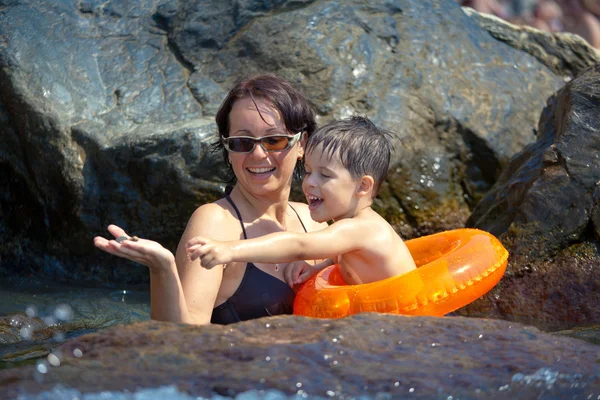 Äiti leikkii poikansa kanssa lähellä kivistä rantaa. — kuvapankkivalokuva