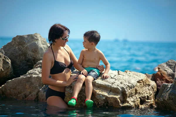 Mor talar med sin son på en stenig havsstrand — Stockfoto