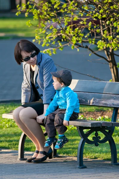 Mãe e filho felizes sentados no banco no parque da cidade — Fotografia de Stock