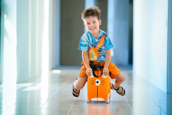 Мальчик смеется и сидит на чемодане в аэропорту — стоковое фото