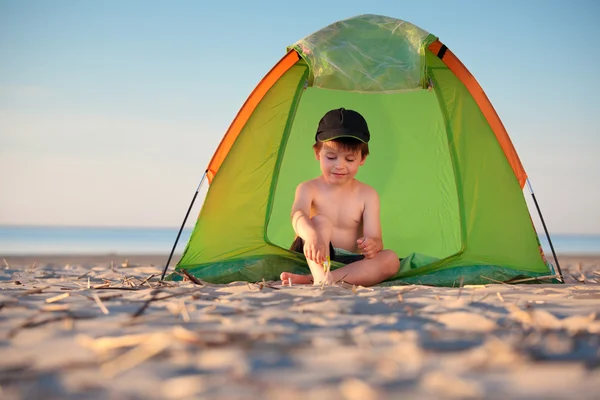 Liten pojke spelar i sitt tält på stranden — Stockfoto