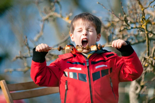 Мальчик с удовольствием ест овощи на гриле — стоковое фото