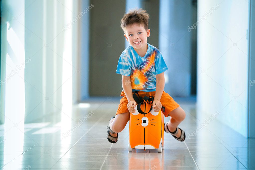 Boy laughs and sitting on a suitcase at airport