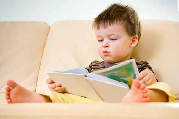 Kleiner Junge liest Buch auf Sofa — Stockfoto