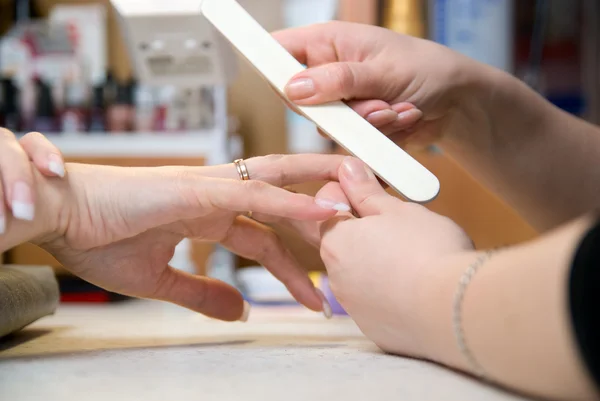 Mãos femininas fazem manicure por nailfile para mulher — Fotografia de Stock