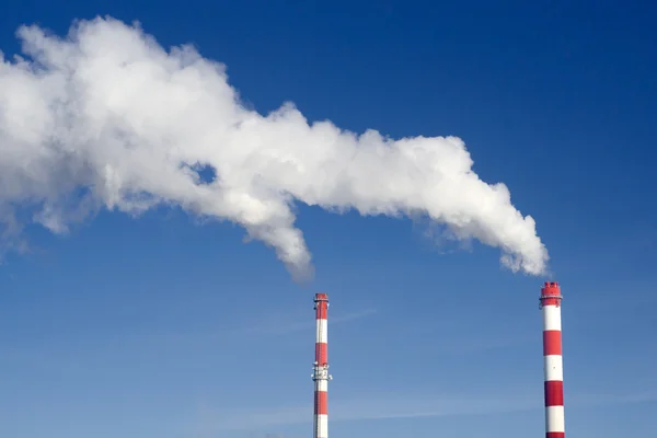 Coppia di camini industriali con tanto fumo su un cielo blu — Foto Stock