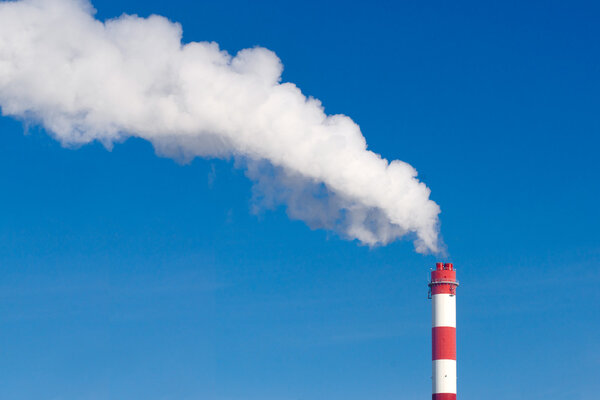 Industrial chimney with lots of smoke on a blue sky