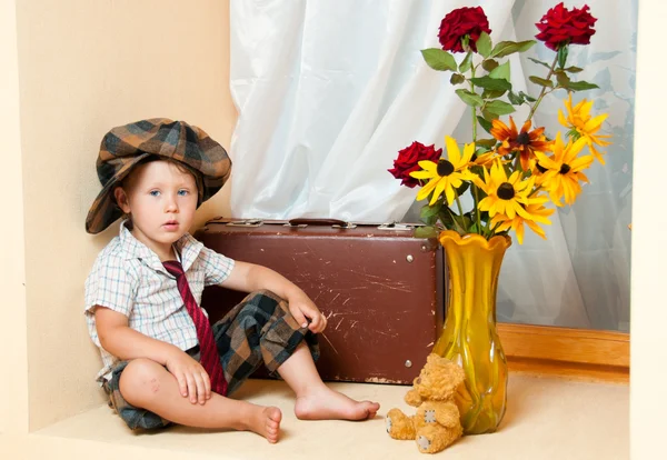 Милый маленький мальчик с цветочком, сидящий на старом чемодане. He i — стоковое фото