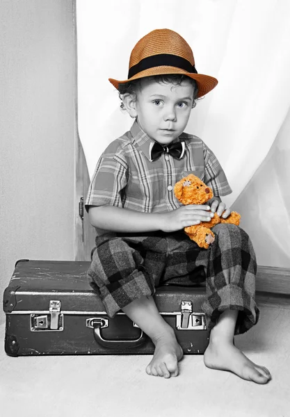 En pojke med en nallebjörn som sitter på en resväska. — Stockfoto