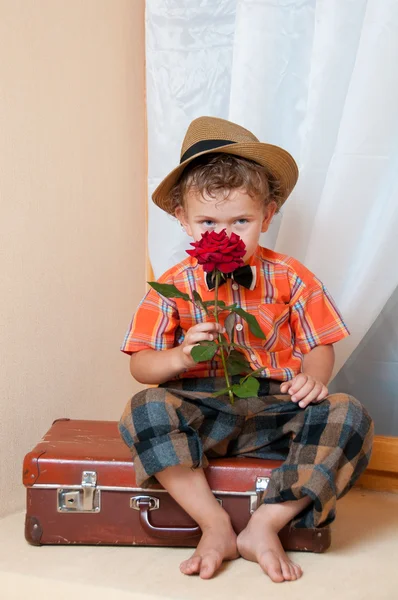 古いスーツケースの上に座って花とかわいい男の子。彼は私は — ストック写真