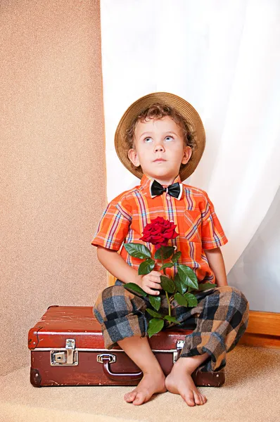 Cute little boy with the flower sitting on an old suitcase. He i — Stock Photo, Image
