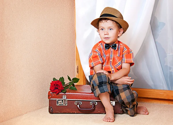 Joli petit garçon avec la fleur assise sur une vieille valise. Il a... — Photo