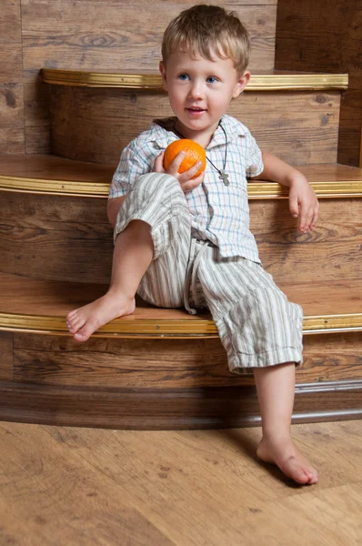 一个可爱的男孩坐在台阶上，他手里的桔子. — 图库照片