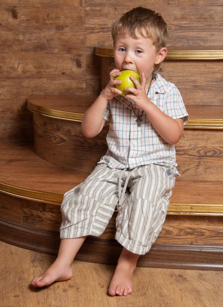 Roztomilý chlapec s jablkem v ruce, sedí na schodech. — Stock fotografie