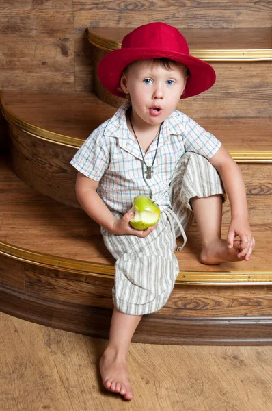 A cute boy with an apple in his hand sitting on the steps. — Stock Photo, Image