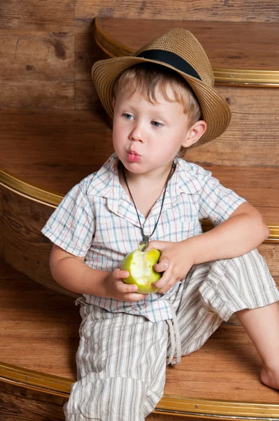 A cute boy with an apple in his hand sitting on the steps. — Stock Photo, Image