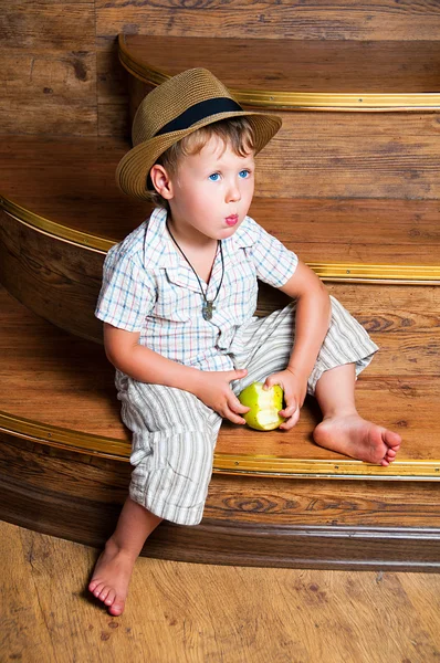 Um menino bonito com uma maçã na mão sentada nos degraus . — Fotografia de Stock