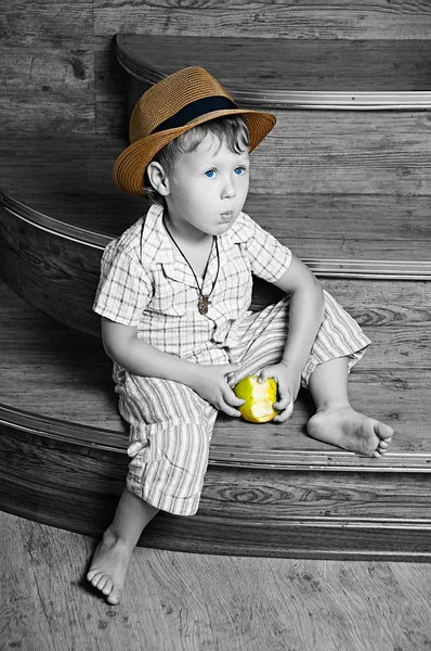 Ένα χαριτωμένο αγόρι με ένα μήλο στο χέρι του καθισμένος στα σκαλιά. — Φωτογραφία Αρχείου