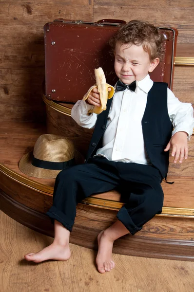 Cute little boy with a banana in his hand sitting on the steps. — Stock Photo, Image