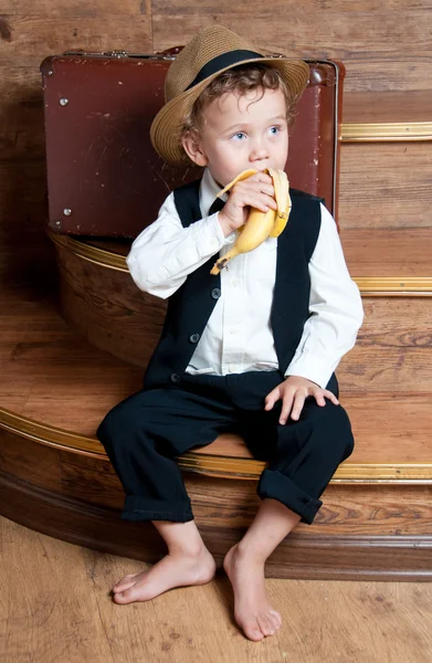 Lindo niño con un plátano en la mano sentado en las escaleras . — Foto de Stock
