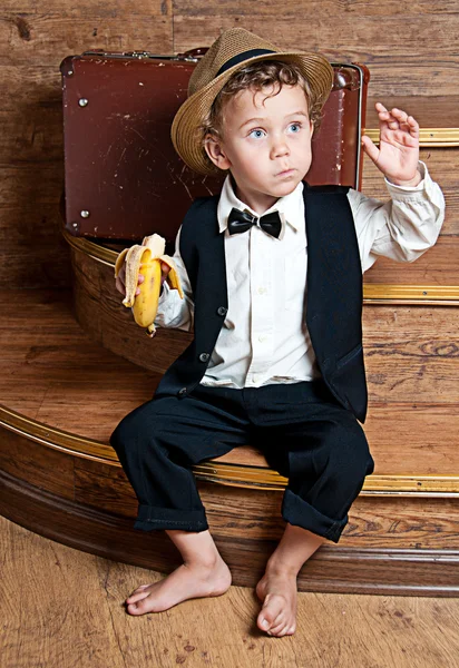 Cute little boy with a banana in his hand sitting on the steps. — Stock Photo, Image