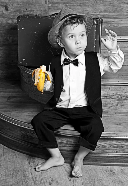 Симпатичный маленький мальчик с бананом в руке сидит на ступеньках . — стоковое фото