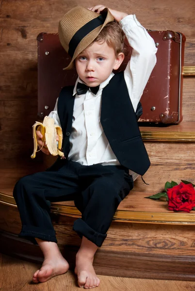 Симпатичный маленький мальчик с бананом в руке сидит на ступеньках . — стоковое фото
