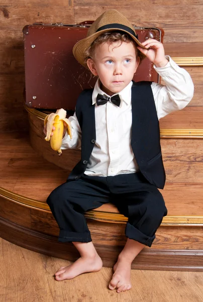 Menino bonito com uma banana na mão sentada nos degraus . — Fotografia de Stock