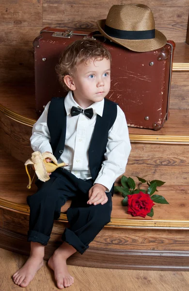 Lindo niño con un plátano en la mano sentado en las escaleras . —  Fotos de Stock