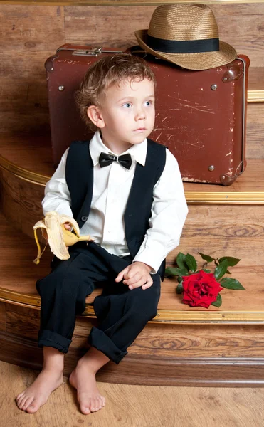 Schattige kleine jongen met een banaan in zijn hand zittend op de stappen. — Stockfoto