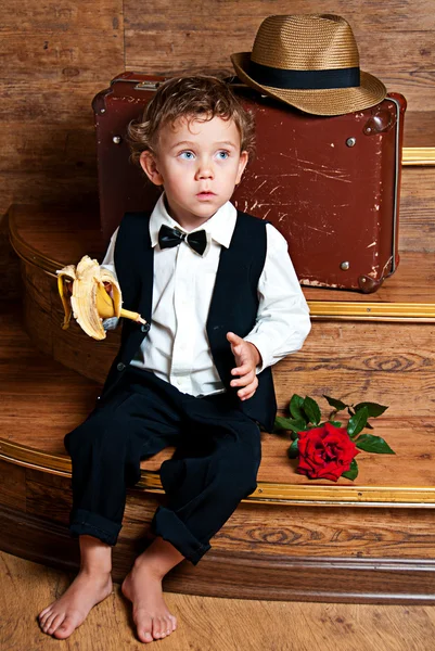 Netter kleiner Junge mit einer Banane in der Hand, der auf den Stufen sitzt. — Stockfoto