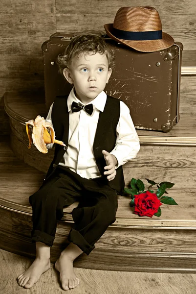 Menino bonito com uma banana na mão sentada nos degraus . — Fotografia de Stock