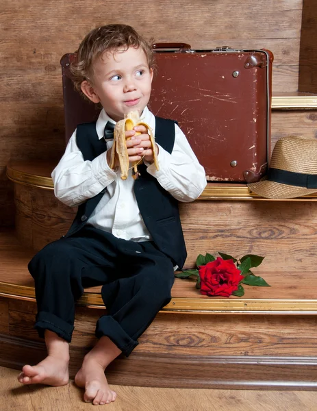 可爱的小男孩坐在台阶上，他手里的香蕉. — 图库照片