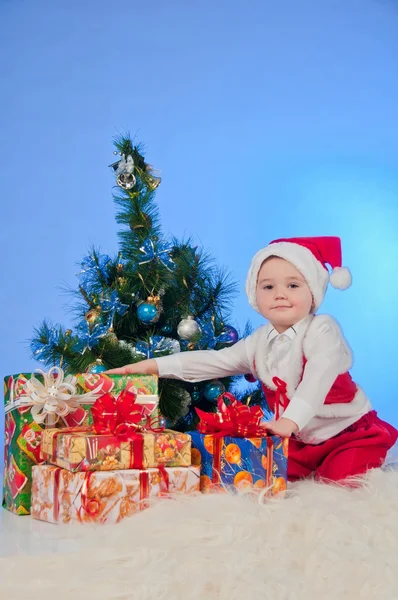 Roliga skrattande bebis i santa kostym med en närvarande låda. — Stockfoto