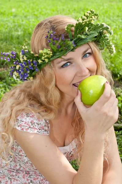 Eine schöne blonde junge Frau mit einem Kranz auf dem Kopf isst — Stockfoto