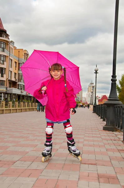 Een meisje op rolschaatsen met een paraplu naar beneden de weg. — Stockfoto