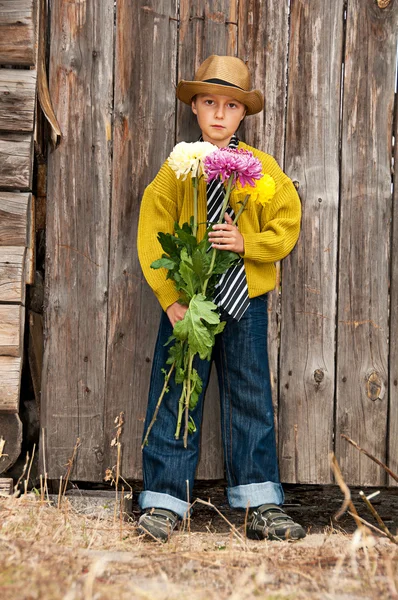 A boy with a bouquet of chrysanthemums against a wooden fence. — Stock Photo, Image