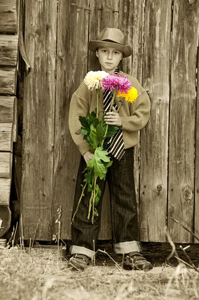 Een jongen met een boeket van chrysanten tegen een houten hek. — Stockfoto