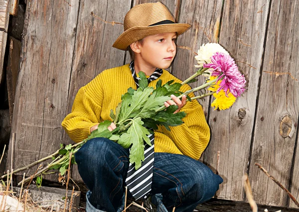 Un niño con un ramo de crisantemos contra una valla de madera . —  Fotos de Stock