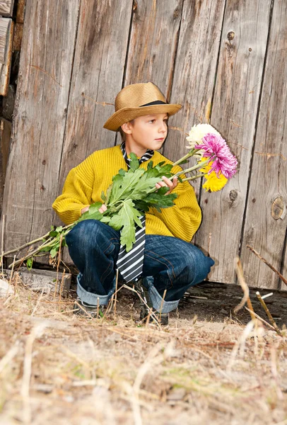 Um menino com um buquê de crisântemos contra uma cerca de madeira . — Fotografia de Stock