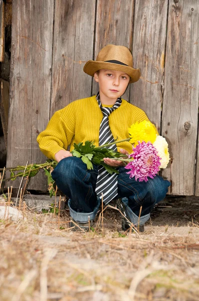 Un garçon avec un bouquet de chrysanthèmes contre une clôture en bois . — Photo
