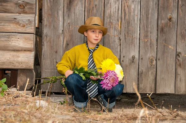 Chlapec s kytici chryzantém proti dřevěný plot. — Stock fotografie