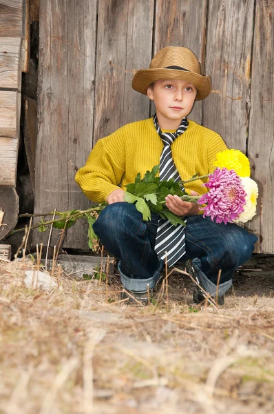 Un niño con un ramo de crisantemos contra una valla de madera . —  Fotos de Stock
