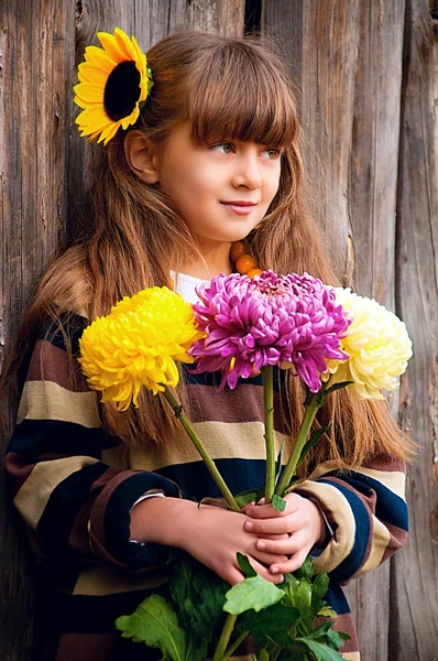A girl with a bouquet of chrysanthemums against a wooden fence. — Stock Photo, Image