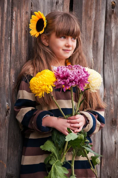 A girl with a bouquet of chrysanthemums against a wooden fence. — Stock Photo, Image