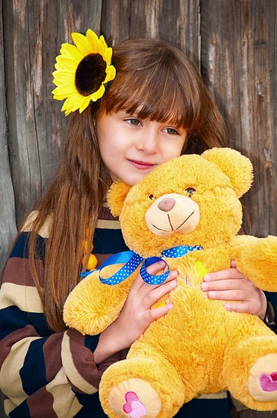 Meisje met teddy bear tegen een houten hek. — Stockfoto