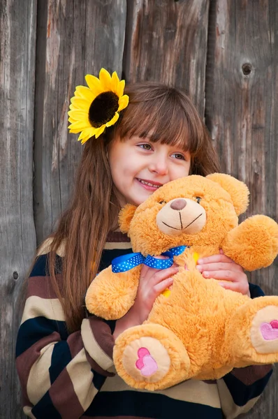 Menina com ursinho de pelúcia contra uma cerca de madeira . — Fotografia de Stock